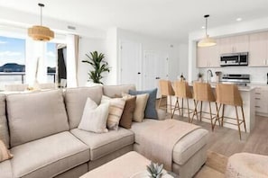 A modern living room with a sectional sofa, a bar area with stools, and a kitchen in the background.