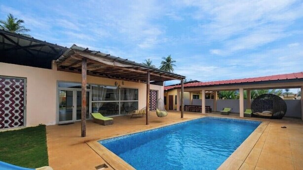 Une piscine avec un patio couvert, une entrée avec une porte vitrée et un espace salon extérieur.