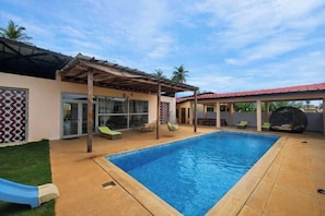 A swimming pool with a covered patio area, a glass door entrance, and outdoor seating.