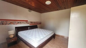 Ein Schlafzimmer mit Holzboden, einem Bett mit Matratze, einem Nachttisch mit Lampe und einem Wandbordüre mit Muster.