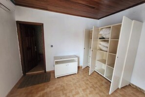 Une pièce avec un plafond en bois, une armoire blanche dont les portes sont ouvertes et un petit meuble blanc.