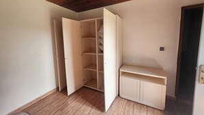Ein Zimmer mit Holzbalkendecke, einem weißen Kleiderschrank mit geöffneten Türen und einem kleinen weißen Schrank.