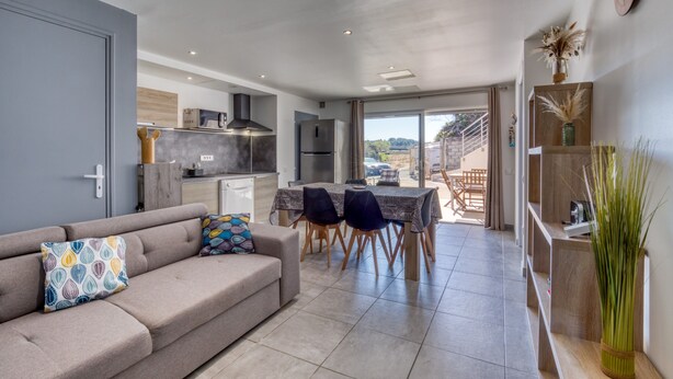 A modern interior with a sofa, dining table, chairs, and a kitchen area. - "Villa Athena" Cottage with Shared Pool, Private Terrace, and Wi-Fi (Montagnac)