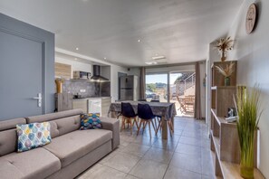 A modern interior with a sofa, dining table, chairs, and a kitchen area. - "Villa Athena" Cottage with Shared Pool, Private Terrace, and Wi-Fi (Montagnac)