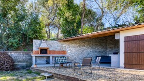 A patio with a stone wall, a brick oven, outdoor seating, and a wooden deck. - "Villa Athena" Cottage with Shared Pool, Private Terrace, and Wi-Fi (Montagnac)