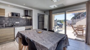 A modern kitchen with a dining area, a built-in microwave, a stainless steel refrigerator, and a large sliding glass door leading to an outdoor patio. - "Villa Athena" Cottage with Shared Pool, Private Terrace, and Wi-Fi (Montagnac)