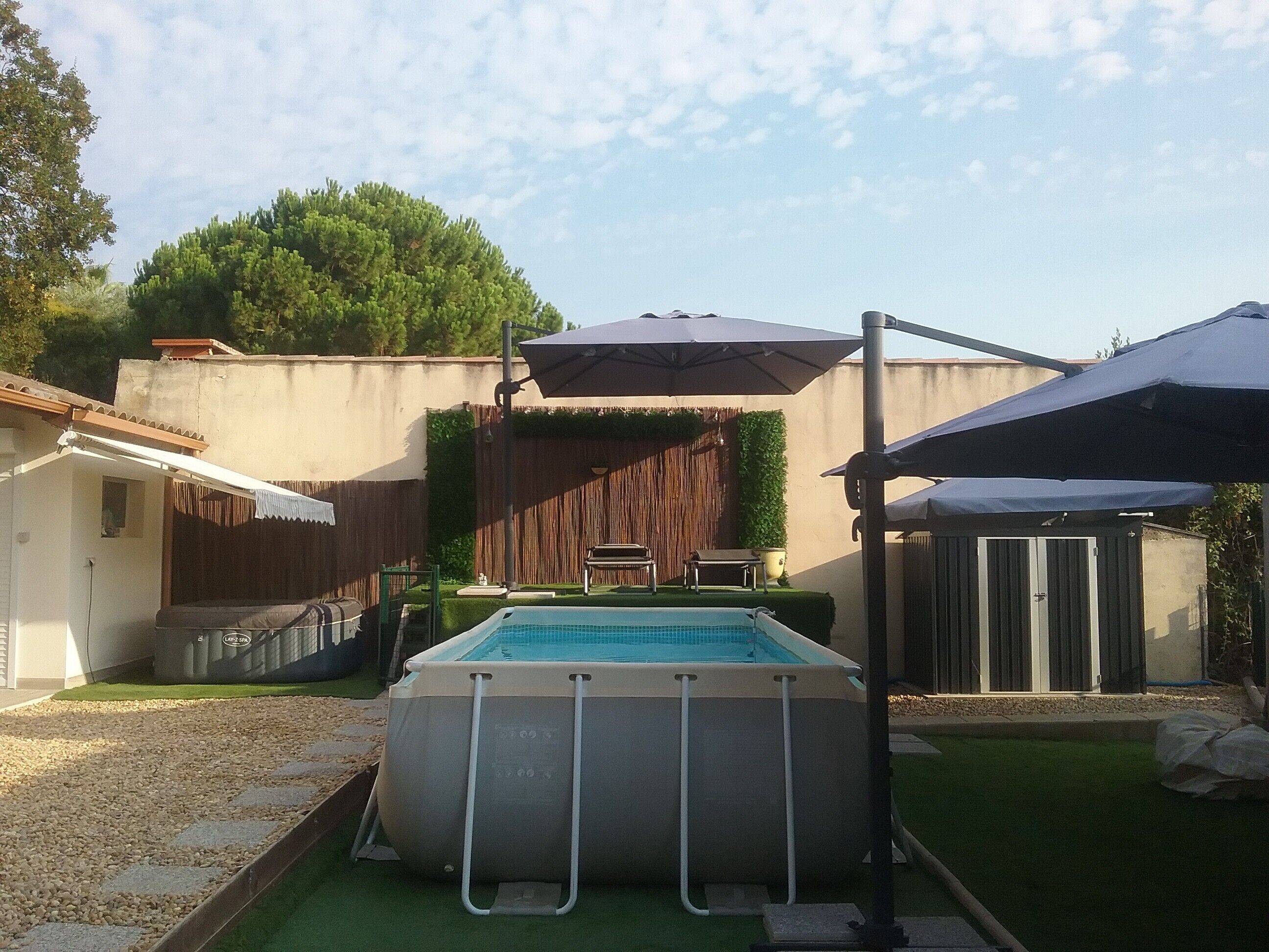 Ein Swimmingpool mit einer Leiter, umgeben von einem Holzzaun, einer Pergola und einer kleinen Terrasse.