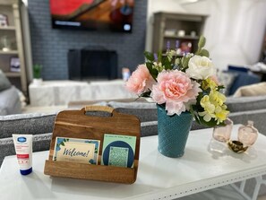 Un área de recepción con un letrero de bienvenida de madera, dispensador de gel antibacterial y un jarrón con flores.