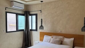 Un dormitorio con cama, ventana con cortinas, equipo de aire acondicionado y lámpara colgante.