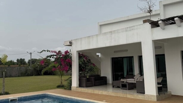 Una casa moderna con un porche cubierto, mobiliario exterior y una piscina.