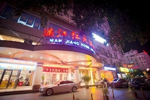 A hotel with a curved facade, signage in multiple languages, and a parking area in front. - Man Jiang Hong Hotel (Nanning)