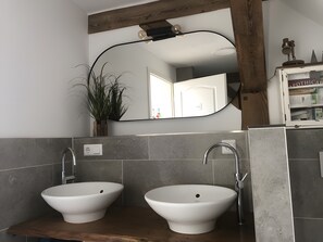 Une salle de bain avec deux vasques blanches, un comptoir en bois, un grand miroir et une plante.