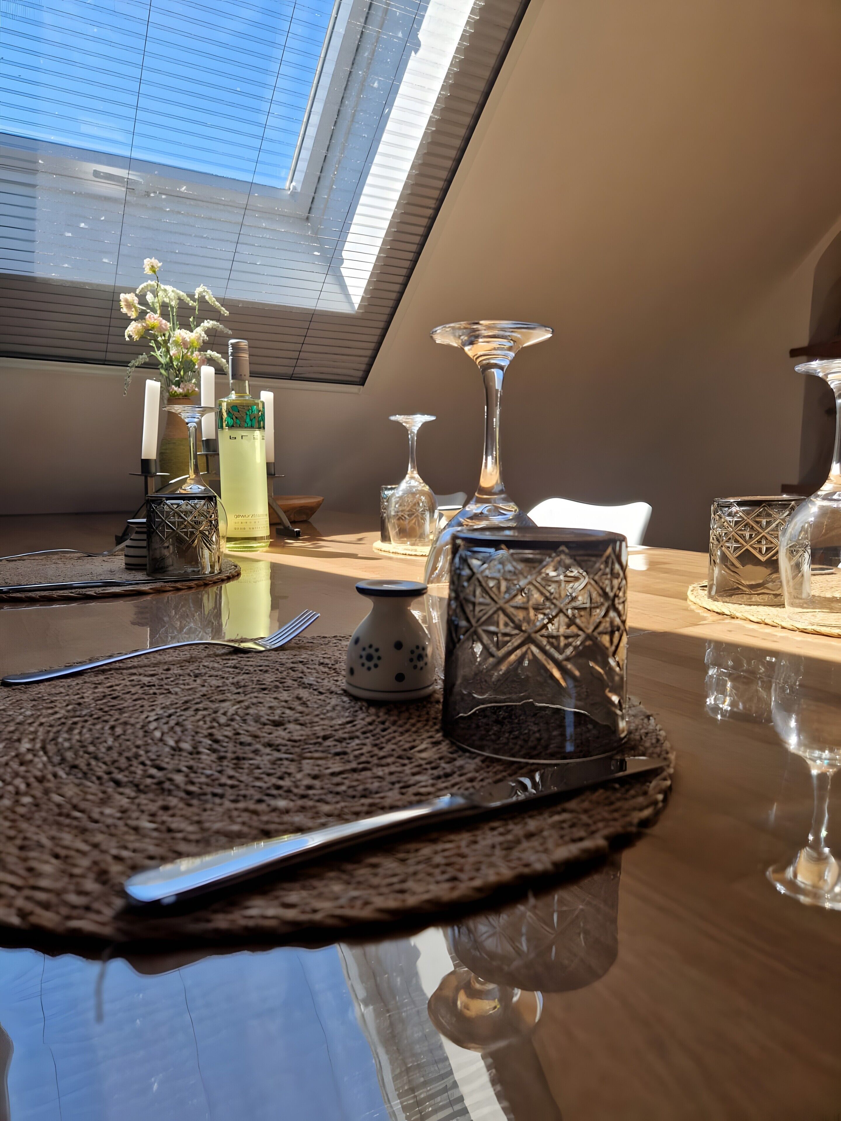 Ein Esstisch mit freiem Blick auf den Himmel durch ein Oberlicht, eine Vase mit Blumen und verschiedene Gläser.