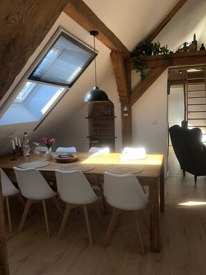 A dining area with a wooden table, white chairs, a hanging pendant light, a skylight, and a wooden beam structure. - Apartment 'Lale' with Lake View, Shared Terrace and Wi-Fi (Wustrow)