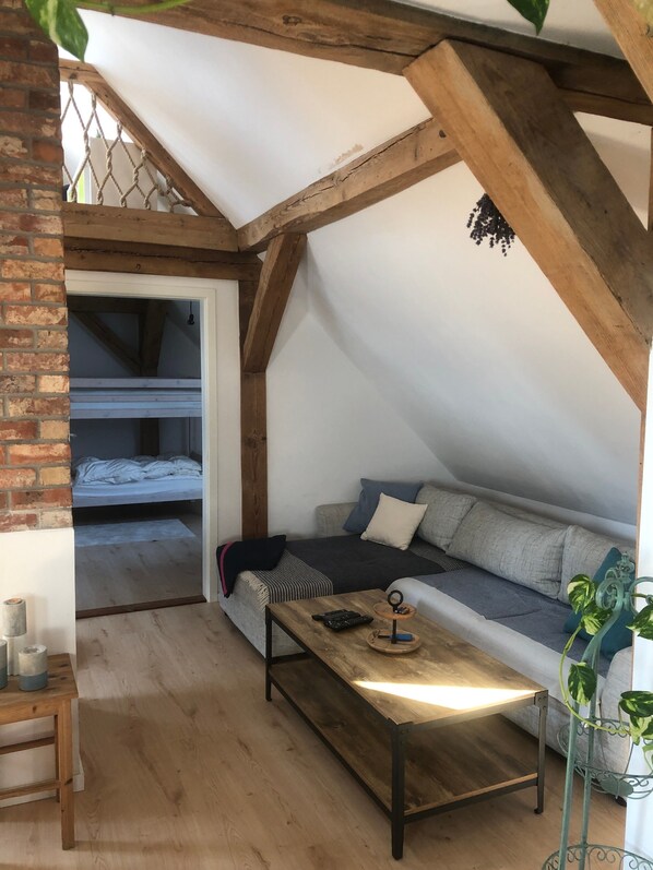 A loft-style bedroom with exposed wooden beams, a bunk bed, a sofa, a coffee table, and a potted plant.
