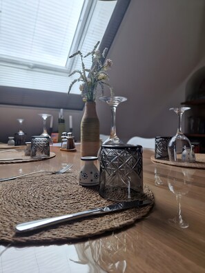 Une table à manger agrémentée d’un set de table en fibres tressées, d’un vase avec des fleurs et de divers objets en verre.
