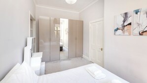 Une chambre moderne avec un lit, une armoire blanche et des œuvres d’art abstraites accrochées au mur.