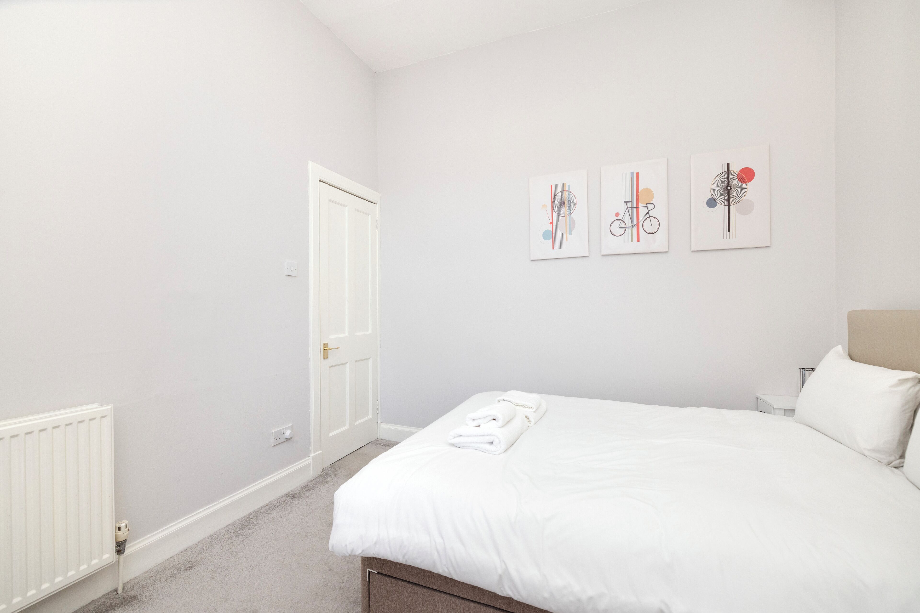 Une chambre à coucher avec un lit, des murs blancs et trois œuvres d’art accrochées au mur.