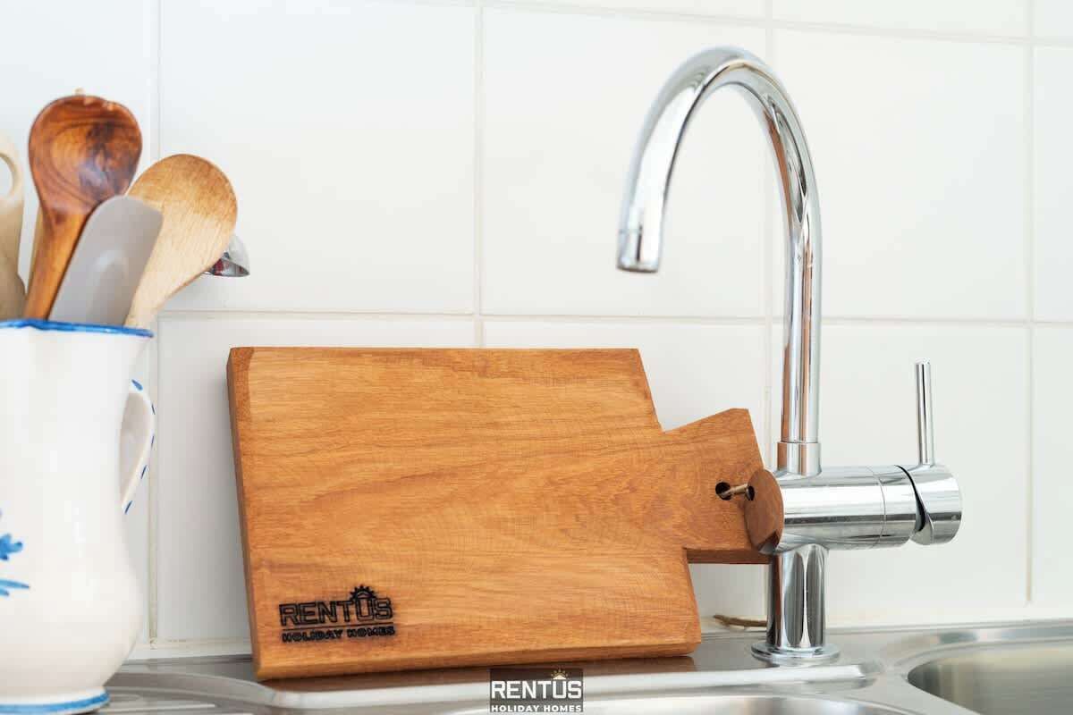 A kitchen with a wooden cutting board, a stainless steel faucet, and a cup with wooden utensils.