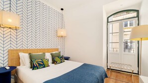 Een hotelkamer met een bed, nachtkastje, lamp, raam en deur.
