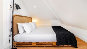 Ein Einzelbett mit Holz-Kopfteil, weißer Bettwäsche, einer schwarzen Decke und einer Wandlampe.