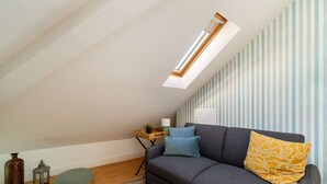 Ein Loft-Zimmer mit schrägem Dach, einem grauen Sofa, einem kleinen Tisch und einer gestreiften Wand.