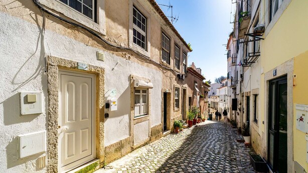 A narrow cobblestone street lined with buildings, some with balconies and potted plants. - Alfama Retreat Steps from Santa Luzia Viewpoint (Lisbon)