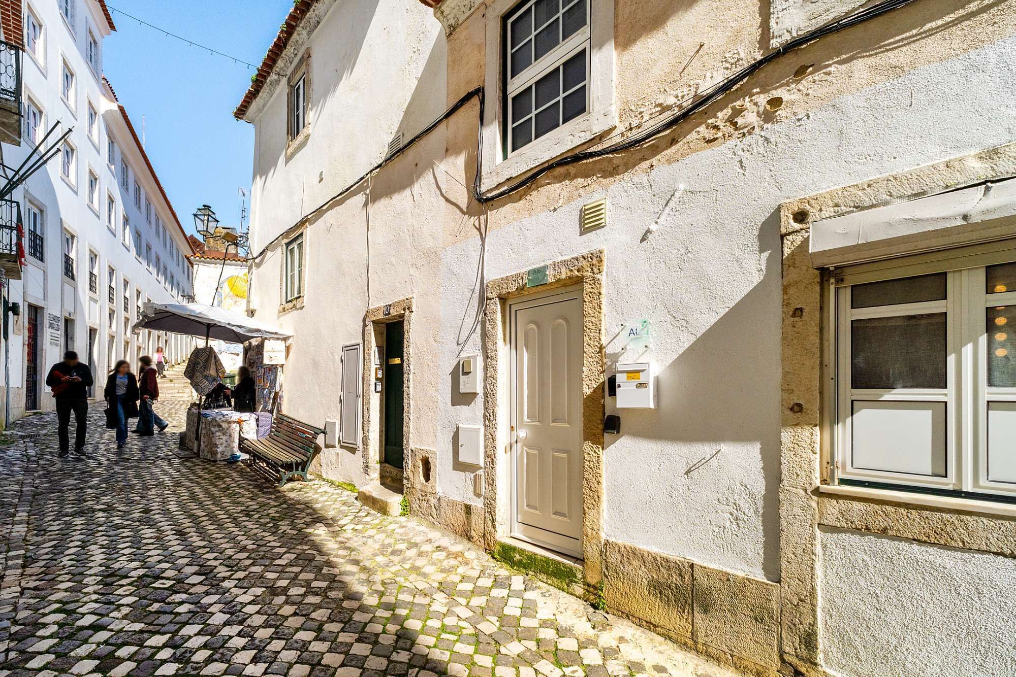 A cobblestone street with buildings, a bench, and a door with a sign.