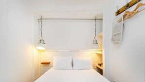 A narrow room with a bed centered, white walls, a small wooden shelf, and a hanging light fixture. - Alfama Retreat Steps from Santa Luzia Viewpoint (Lisbon)