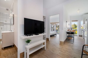 A modern living room with a flat-screen TV on a white stand, a small plant, and a bench. - Porto Bonfim Retreat — Modern & Comfortable (Porto)
