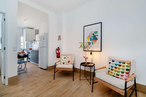 Ein modernes Wohnzimmer mit Küche im Hintergrund, einem Feuerlöscher und einem gerahmten abstrakten Kunstwerk an der Wand.