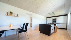 Eine moderne Küche mit einer zentralen Kochinsel, Holzböden und einem Essbereich mit rundem Tisch und Stühlen.