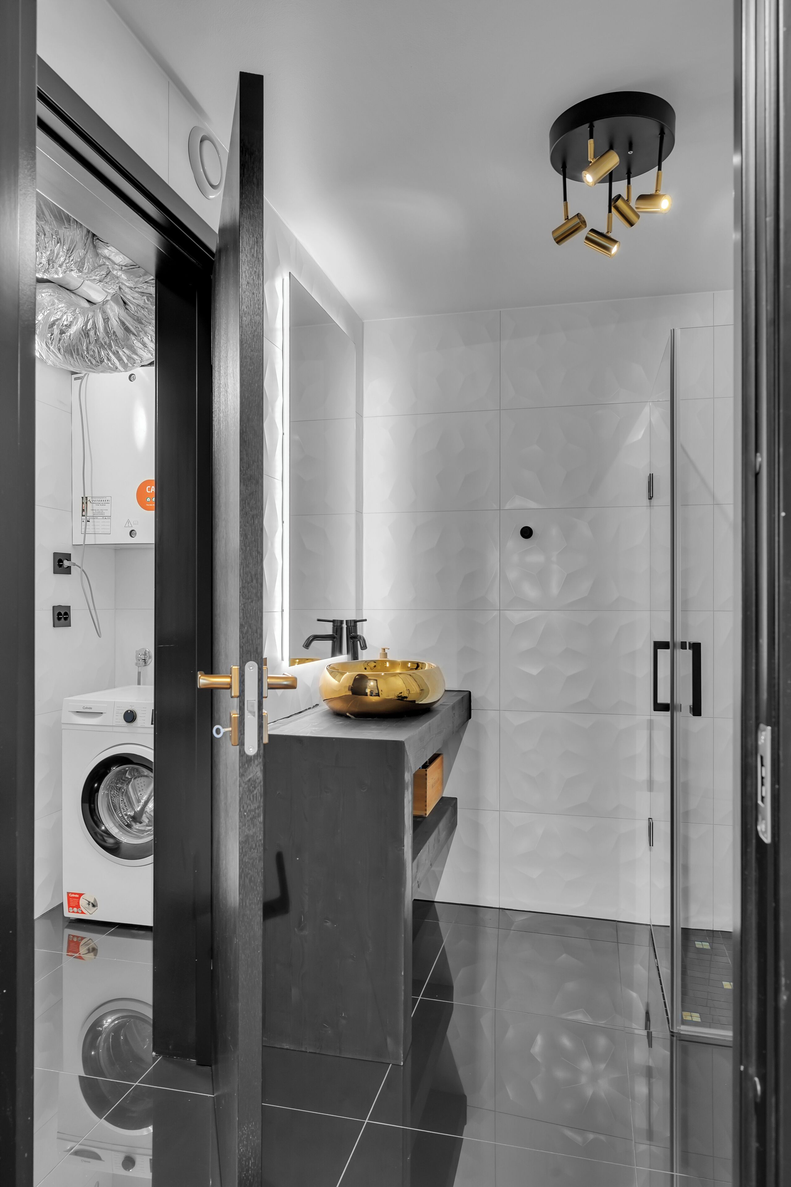 A modern bathroom with a glass shower enclosure, a black door, and a gold sink.