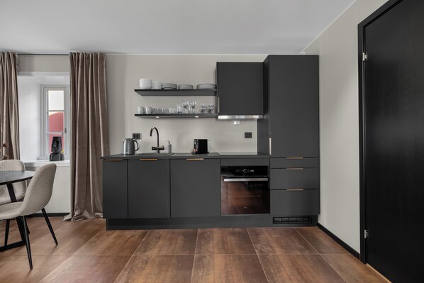 Une cuisine moderne avec des meubles de couleur sombre, un four encastré et un coin repas comprenant une table et des chaises.