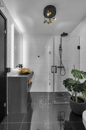 Une salle de bain moderne avec une douche à parois de verre, un lavabo noir avec un receveur jaune et une plante en pot.