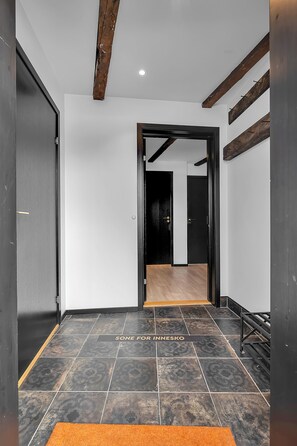 Un corridoio con piastrelle scure a motivi decorativi, pavimento in legno e una porta nera che dà su un'altra stanza.
