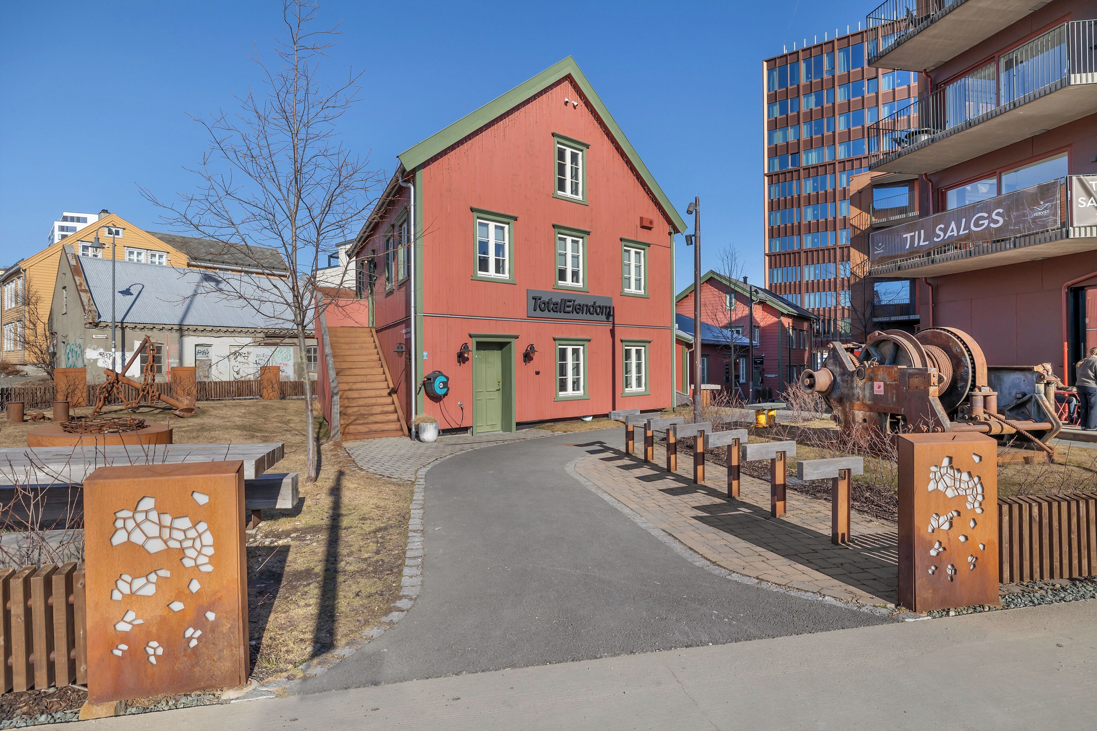 Un bâtiment rouge avec une porte verte portant l’inscription « TotalEllendomy », et, au fond, un bâtiment moderne doté de balcons sur lesquels on peut lire « TIL SALGS ».