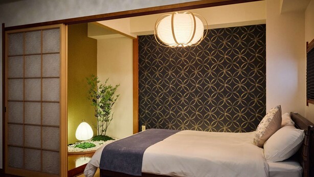 A traditional Japanese-style bedroom with a sliding shoji screen door, a bed with white bedding, and a patterned wallpaper. - Ikebukuro 11-min walk | Private 6BR home | 77㎡, 2 baths | Ideal Tokyo base (Toshima-ku)