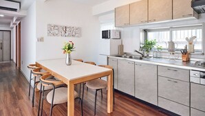 A modern kitchen with a dining area, wooden chairs, a white table, and a vase of flowers. - Ikebukuro 11-min walk | Private 6BR home | 77㎡, 2 baths | Ideal Tokyo base (Toshima-ku)