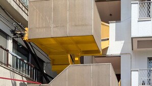 A multi-story building with a yellow and beige color scheme, featuring a covered entrance and a visible fire hose on the ground floor. - Ikebukuro 11-min walk | Private 6BR home | 77㎡, 2 baths | Ideal Tokyo base (Toshima-ku)