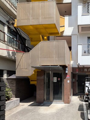A multi-story building with a yellow and beige color scheme, featuring a covered entrance and a visible fire hose on the ground floor. - Ikebukuro 11-min walk | Private 6BR home | 77㎡, 2 baths | Ideal Tokyo base (Toshima-ku)