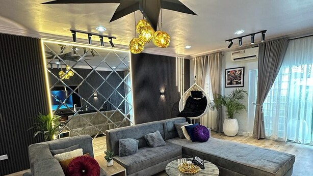 Una sala de estar moderna con una lámpara de techo grande en forma de estrella, un sofá seccional gris, una mesa de centro redonda y un sillón colgante.