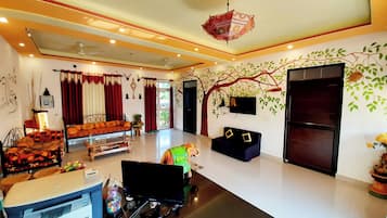 A spacious living room with a sofa, a television, and a decorative tree mural on the wall.