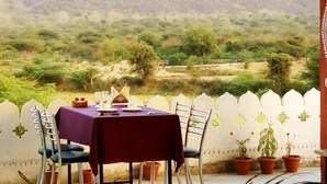 Une table à manger recouverte d’une nappe rouge, avec des chaises et des plantes en pot.