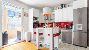Een moderne keuken met witte kastjes, een roestvrijstalen koelkast en een eethoek met een tafel en rode stoelen.