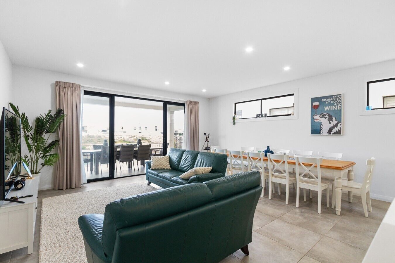 A modern living room with a green sofa, dining table, and chairs, a TV, and a large window with curtains.