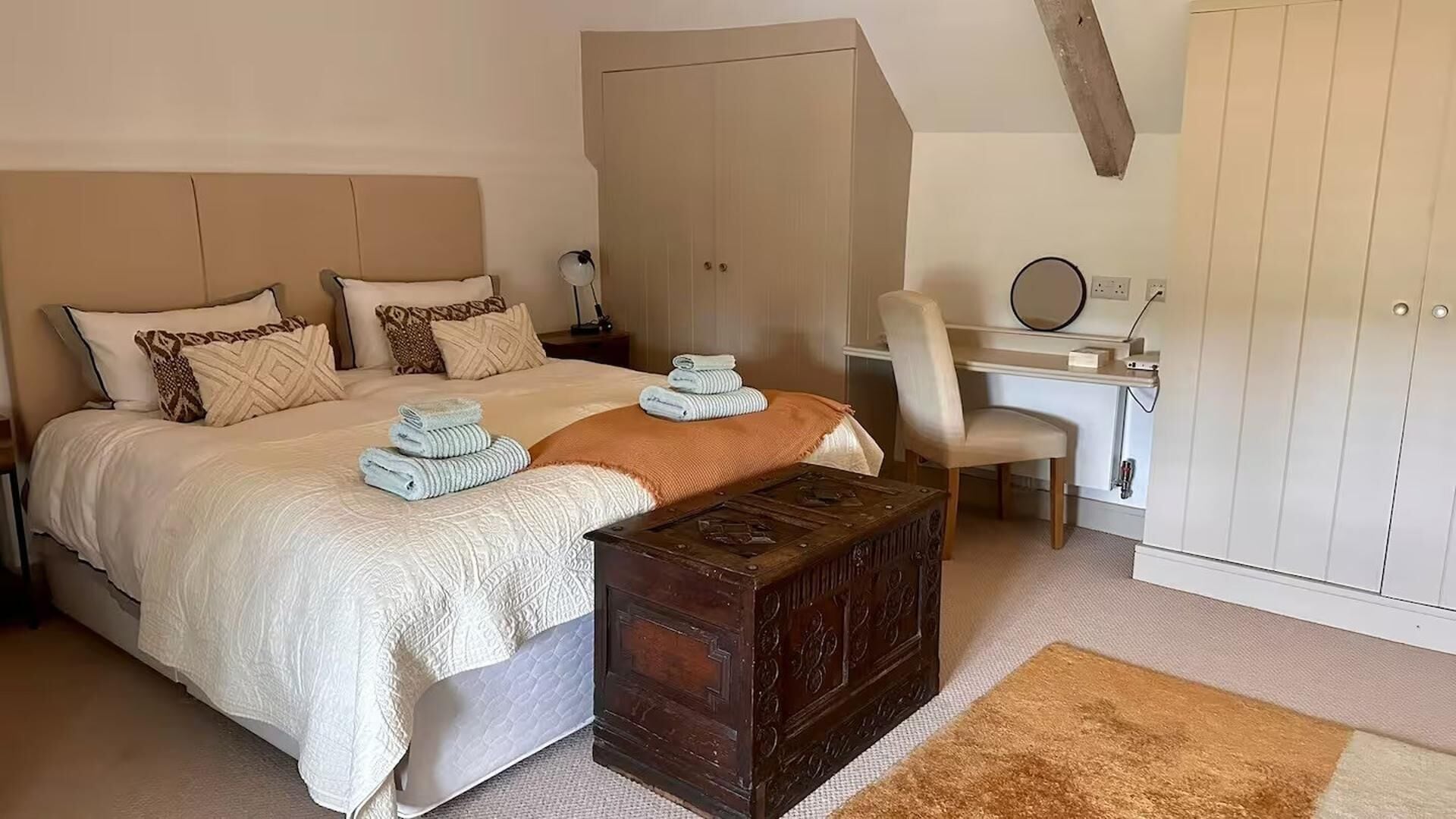 A bedroom with a bed, bedside table, desk, chair, wardrobe, and a small wooden chest.