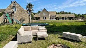 A stone building with a children's play area, including a slide and climbing wall, and a swimming pool area with lounge furniture. - Stunning 6 Bedroom Riverside Barn Cotswold Mill (Cirencester)