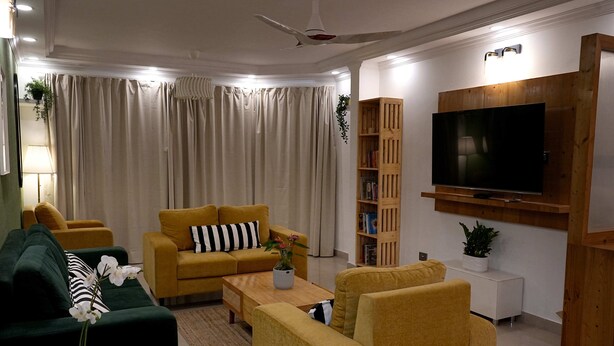 Een woonkamer met een bank, fauteuils, een salontafel, een televisie en een boekenkast.