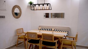Een eetruimte met een rechthoekige tafel, vier houten stoelen met beklede zitplaatsen, een bank met een gestreepte kussen, een spiegel en een hanglamp.